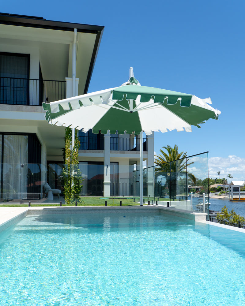 Large green and white umbrella over a pool with a house and garden in the background