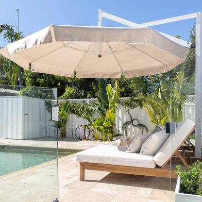 Beige patio umbrella over a lounge chair by a pool with a garden view.
