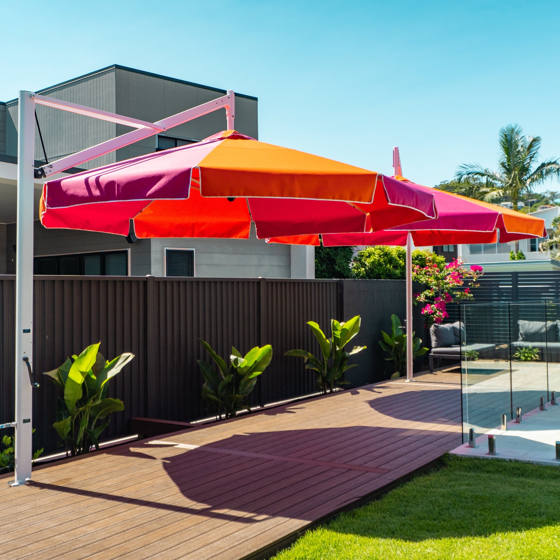 Colorful patio umbrella on a stand in a backyard setting with a pool and house in the background.