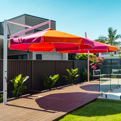 Colorful patio umbrella on a stand in a backyard setting with a pool and house in the background.