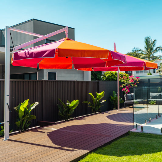 Colorful patio umbrella on a stand in a backyard setting with a pool and house in the background.